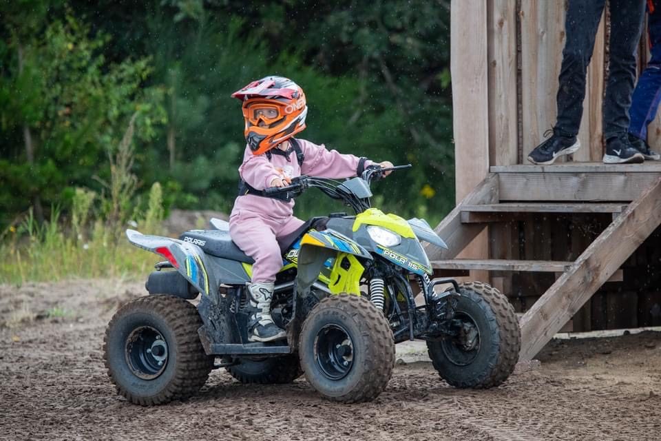 Lille barn i lyserødt tøj og orange hjelm på en lille Polaris ATV